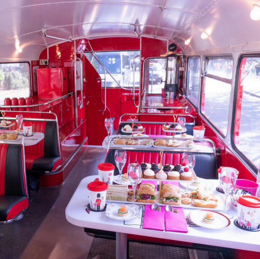 Monopoly Afternoon Tea London bus, themed Monopoly bus tour, London sightseeing bus interior, Monopoly cocktail on board, gourmet afternoon tea spread, interactive Monopoly games onboard, London landmarks through bus windows, celebratory party on Monopoly bus, double-decker bus tour London, Monopoly themed entertainment on bus